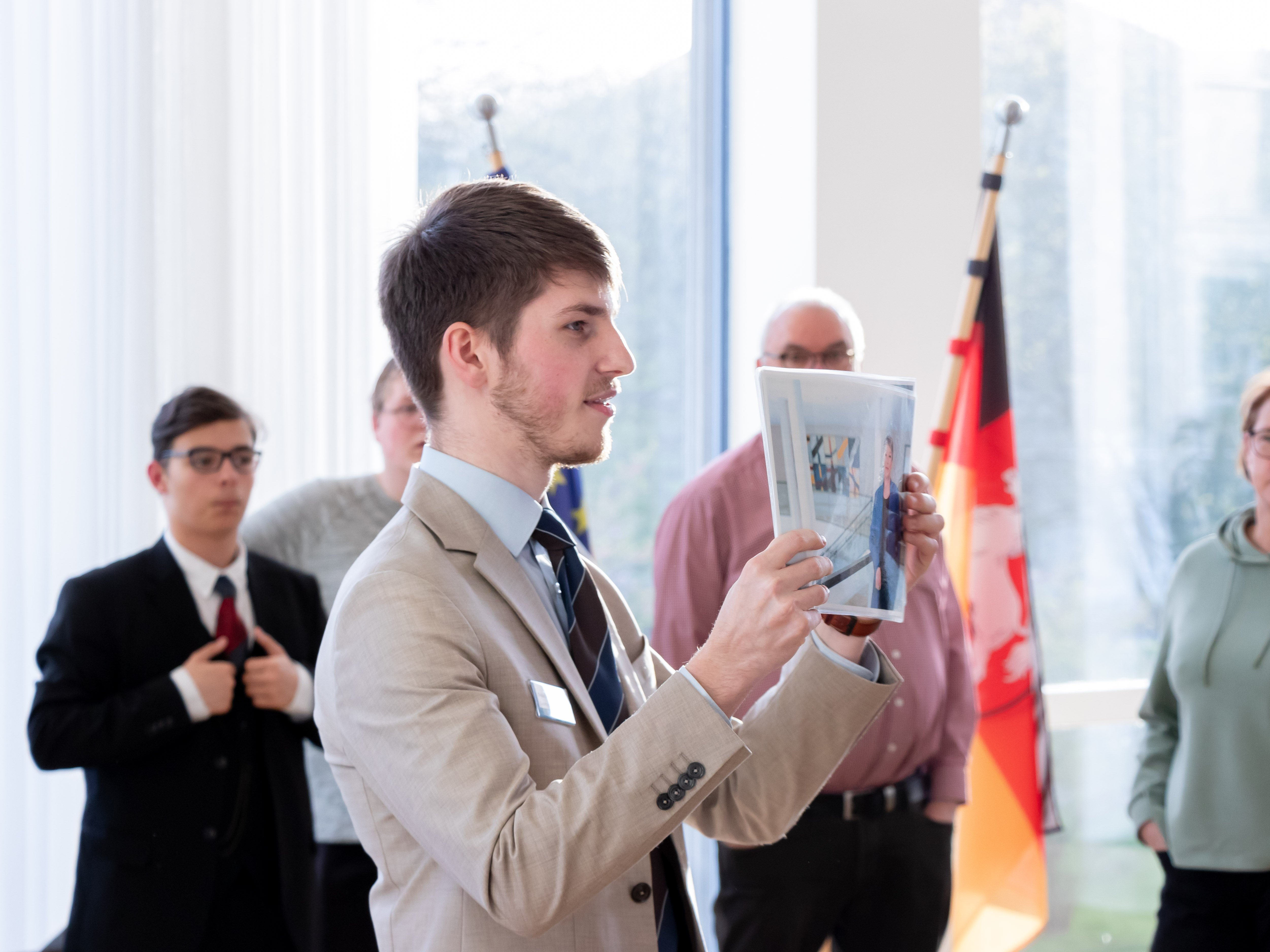Ein Landtagslotse steht im Arbeitszimmer der Landtagpräsidentin und hält ein Foto von ihr hoch. Im Hintergrund sieht man einige Besucherinnen und Besucher.